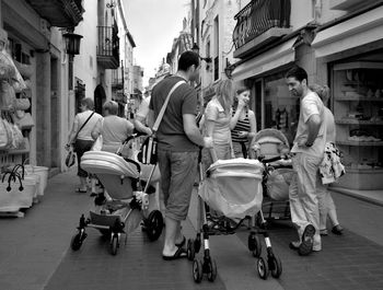 Men and women with baby carriage on street amidst buildings