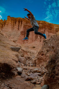 Low angle view of man jumping on rock against sky