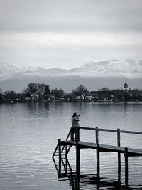 Man standing on pier over lake against sky