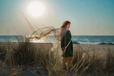 Young woman standing at beach against sky