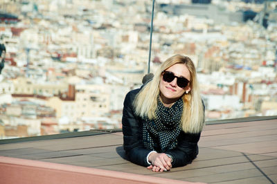 Portrait of young woman lying against cityscape