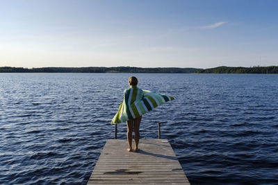 Rear view of man standing on pier over lake against sky