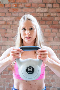 Blonde young muscular womandoing high pull exercise with kettlebells training at the garage gym.