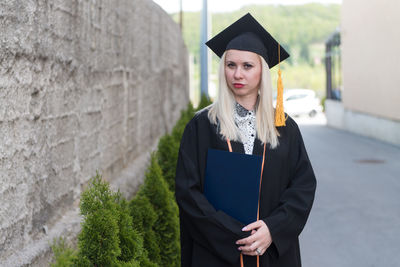 Portrait of woman wearing graduation gown standing against sky