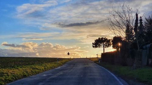 Road amidst trees on field against sky at sunset