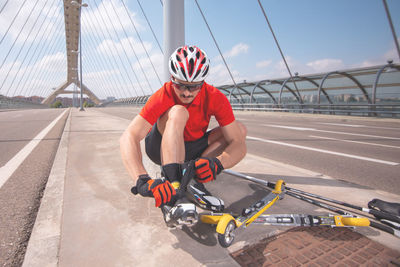 Man repairing push scooter on bridge against sky