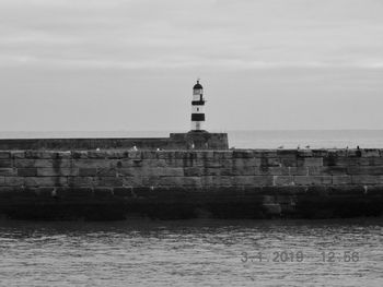 Lighthouse on building by sea against sky