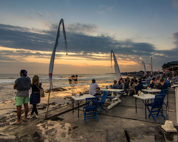 People standing on beach against sky during sunset