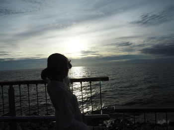 Woman standing by railing against sea during sunset