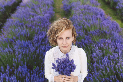 Portrait of woman holding lavenders while standing on field