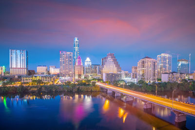 Reflection of illuminated buildings in river against sky