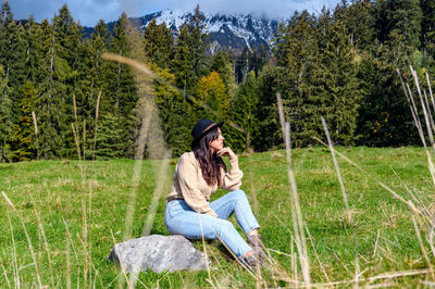 Young woman sitting in the middle of a green pasture in mountains.