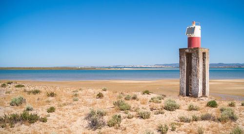 Lighthouse by sea against clear blue sky