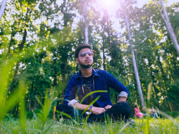 Low angle view of young man wearing sunglasses sitting on land in forest
