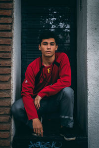 Portrait of young man sitting amidst wall