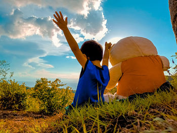 Rear view of boy with arms outstretched by stuffed toy against sky