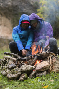 Cyclists arranging halt and warming at fireplace preparing sausages on stick at green meadow in cold day