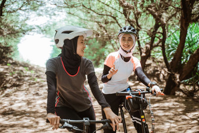 Smiling females with bicycle against trees