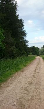 Dirt road amidst field against sky