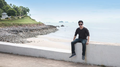 Young man sitting on shore against sky