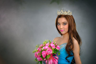 Portrait of beautiful young woman holding bouquet while standing against gray background