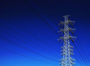 Low angle view of electricity pylon against clear blue sky