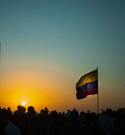 Silhouette of people by flag against sky during sunset