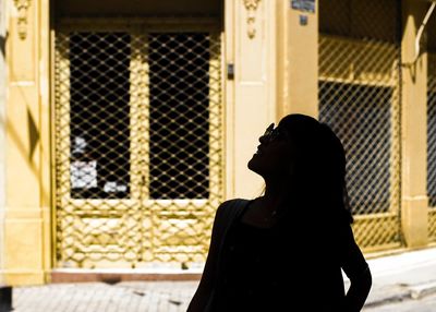 Silhouette of woman looking away while standing against building