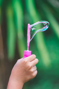 Close-up of hand holding bubble wand against plants