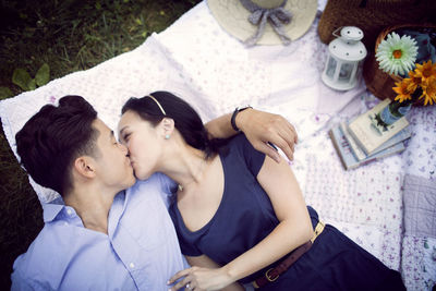 Overhead view of couple kissing while lying on field at park