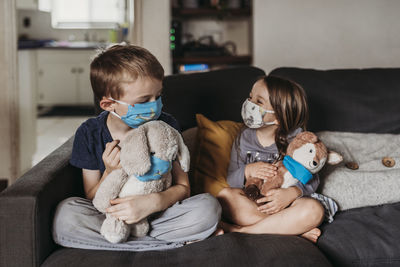 Preschool age girl and school age boy with masks playing toys on couch