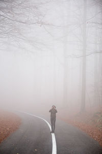 Full length of woman photographing with camera while standing on road in foggy weather