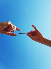 Cropped hand giving marijuana joint to friend against blue sky