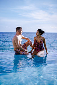 Man and woman sitting in sea against sky