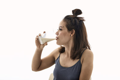 Young woman drinking drink against white background