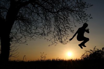 Silhouette man jumping on field against sky during sunset