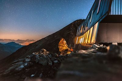 Illuminated house on rocky mountain against star field sky