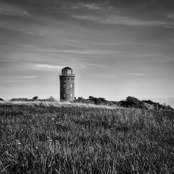 Lighthouse on field against cloudy sky