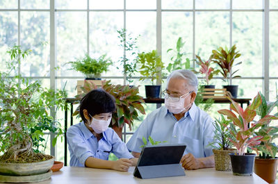 Grandfather spent the holiday with his grandson in greenhouse planting room. both wear face mask.