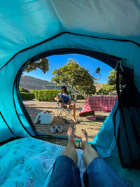 A girl sitting in front of a tent and legs going out of the tent