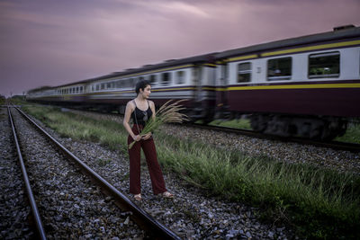 Woman holding plant while standing against train