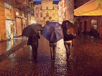 Rear view of female friends standing on wet street in city
