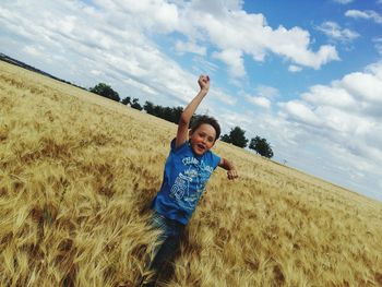 Happy boy standing amidst plants on field against sky