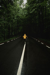 Rear view of child walking on road amidst trees