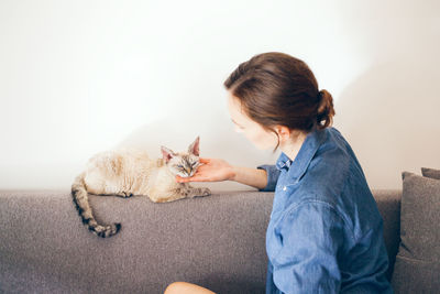 Side view of woman sitting with cat on sofa at home