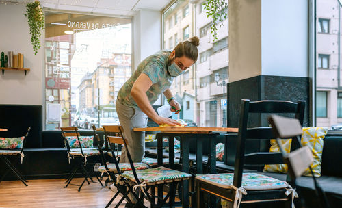 Waiter cleaning table in cafe wearing protective face mask