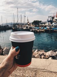 Man holding coffee cup and water against sky