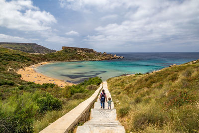 Rear view of mother and son walking towards beach against sky