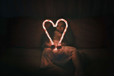 Midsection of woman holding heart shape against black background