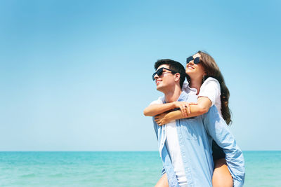 Young woman wearing sunglasses standing by sea against clear sky